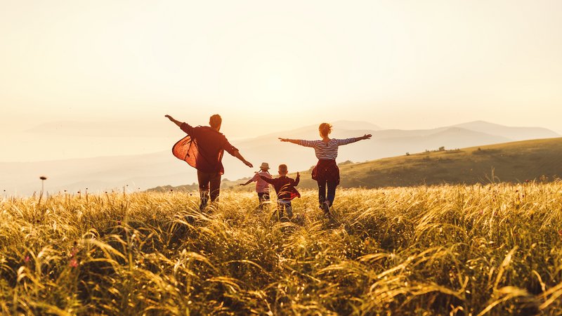 Glückliche Familie: Mutter, Vater, Kinder Sohn und Tochter laufen und springen bei Sonnenuntergang.